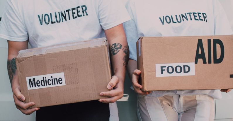 Causes - Man and Woman Carrying Medicine and Food Labelled Cardboard Boxes Behind a White Van